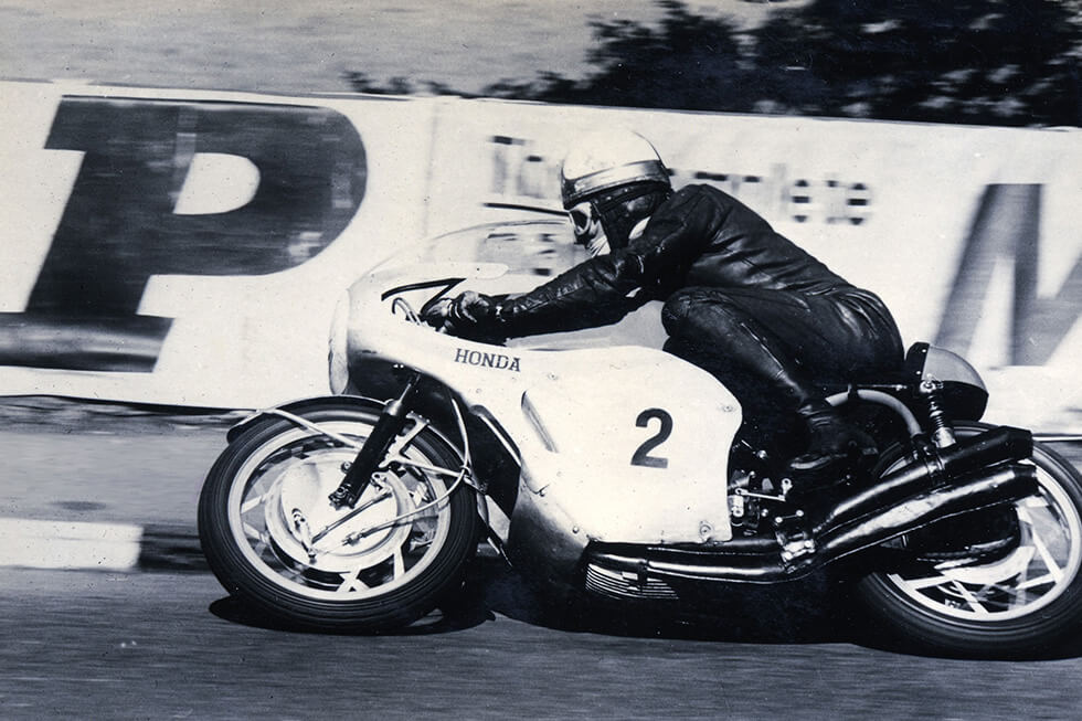 Mike Hailwood riding his air-cooled, 4-stroke, 4-cylinder DOHC engine-powered RC181 at the 1966 Isle of Man TT Races.