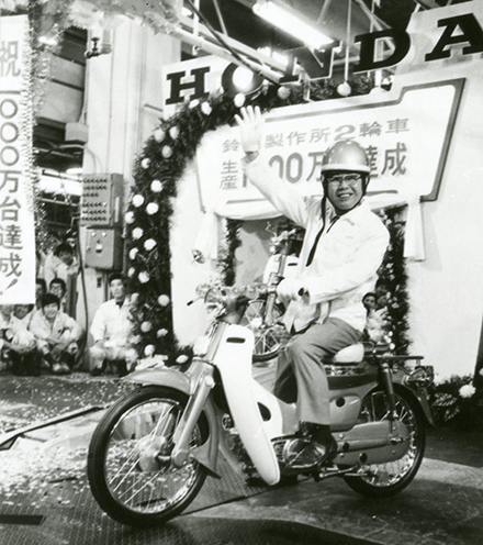 Soichiro Honda beams as he sits on a Super Cub to mark the 10 millionth bike produced at the Suzuka Factory