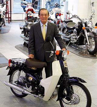 50 years after the first ‘The Soba Is Good, Too, Ma!’ Super Cub ad, Tsugio Ogata, president of Tokyo Graphic Designers, stands with the 50th anniversary edition of the Super Cub (2008)