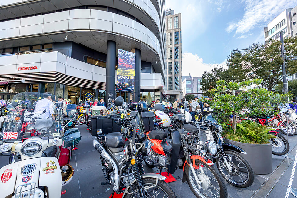 Participants' Super Cubs neatly lined up outside of Honda Welcome Plaza Aoyama, as passersby looked on with great interest. Over the years, the event has become a Autumn tradition in Aoyama.