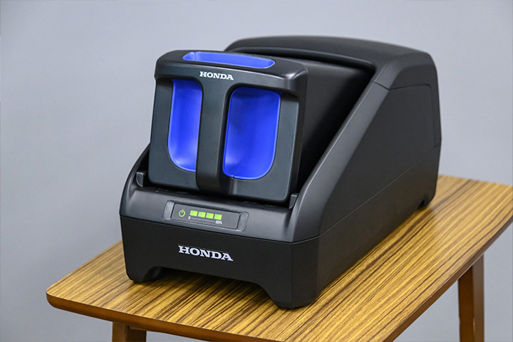 A Honda Mobile Power Pack e: charging up while being placed on and connected to the Honda Power Pack Charger e:. “We are assuming that users will take out the Mobile Power Pack e: from their scooter when they return home and charge it indoors,” said Uchiyama.
