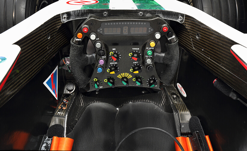 現代のF1マシンらしくカラフルなスイッチボタンが並ぶステアリング。シフトタイミングや路面状況の変化に伴うミクスチャー調整ダイヤルなども見える。上部のLEDパネルにはギヤシフトとレブカウンターが表示される。