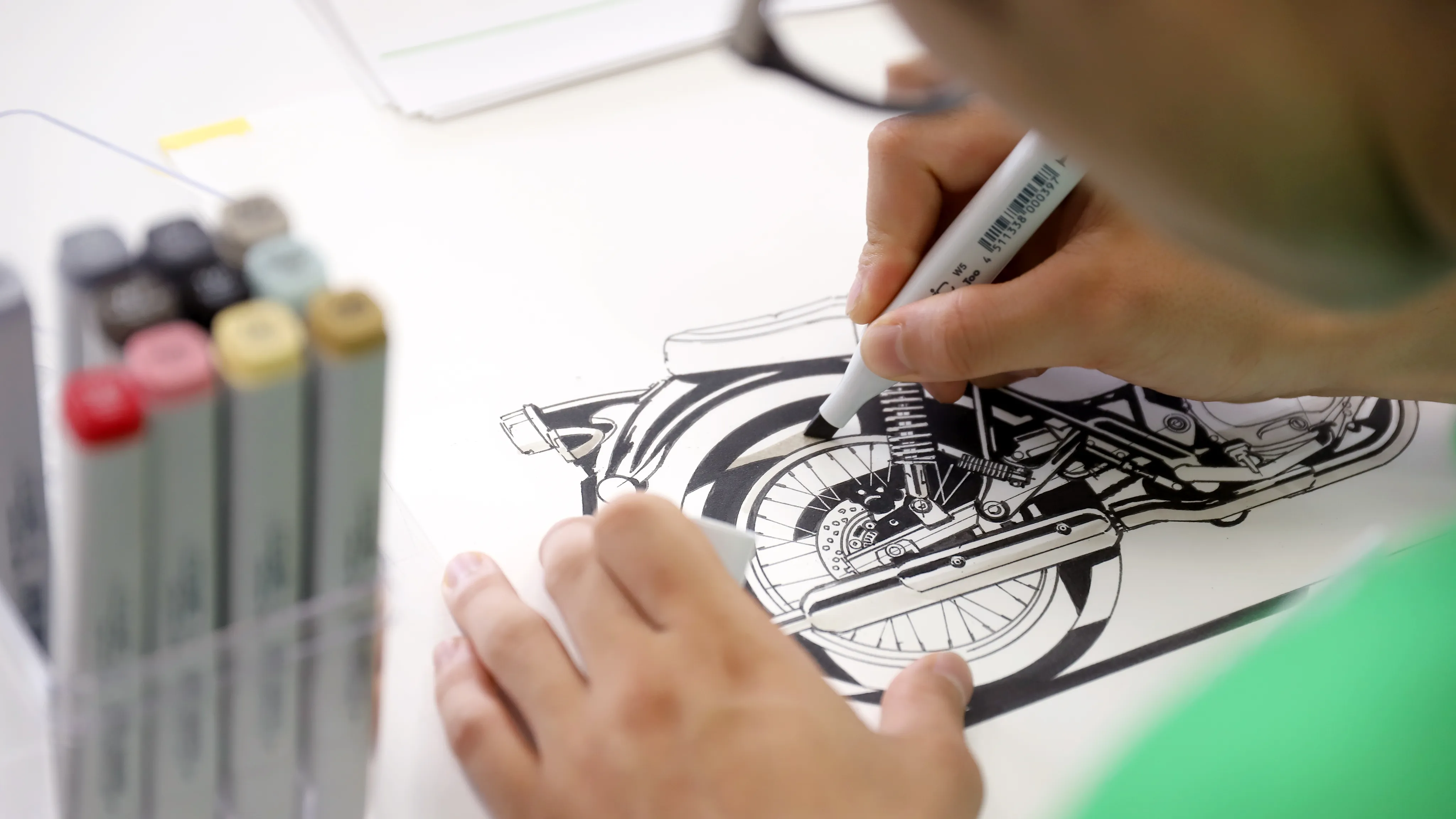 コピックペンでバイクのフィジカルスケッチを描く学生
