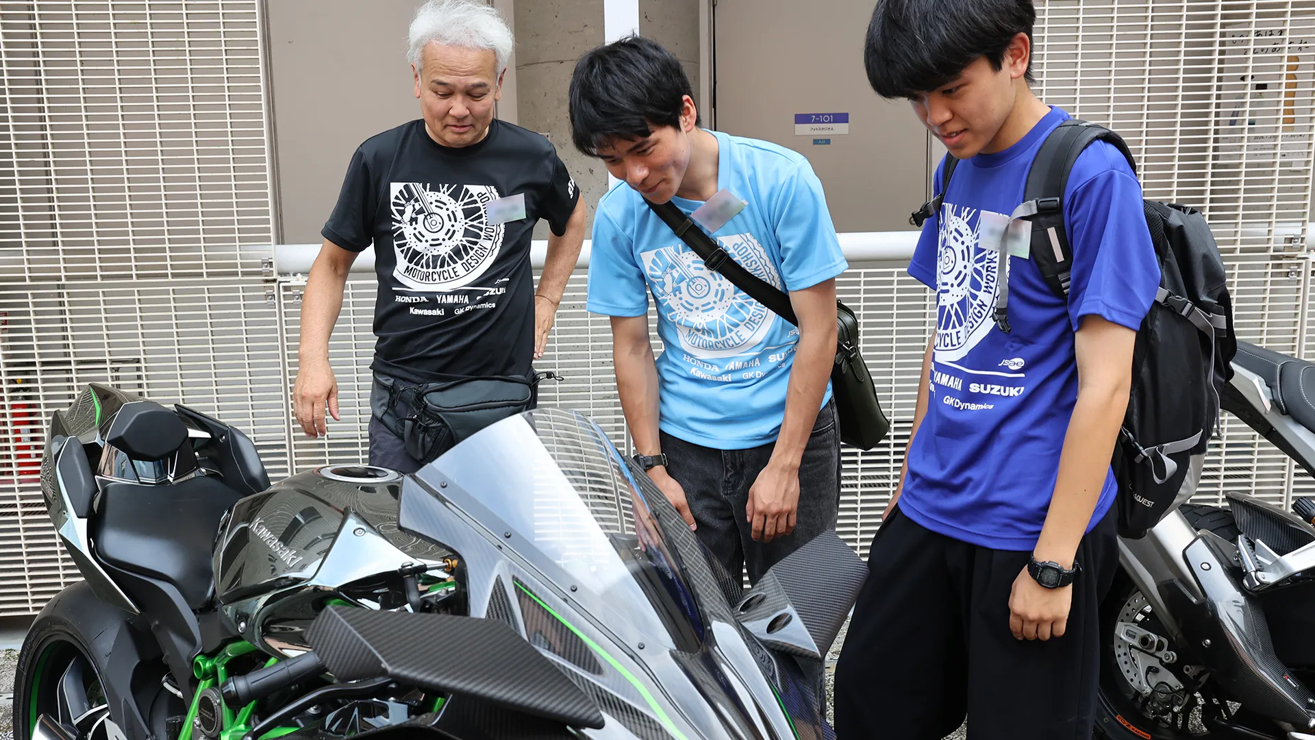 屋外に展示されたKawasakiの車両を前に語り合う講師と学生