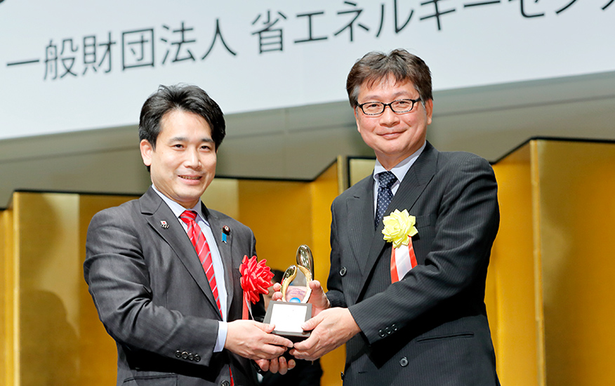 滝波大臣政務官よりトロフィーを手渡されたHonda熊本製作所 生産業務部 中谷俊彦部長（左）。